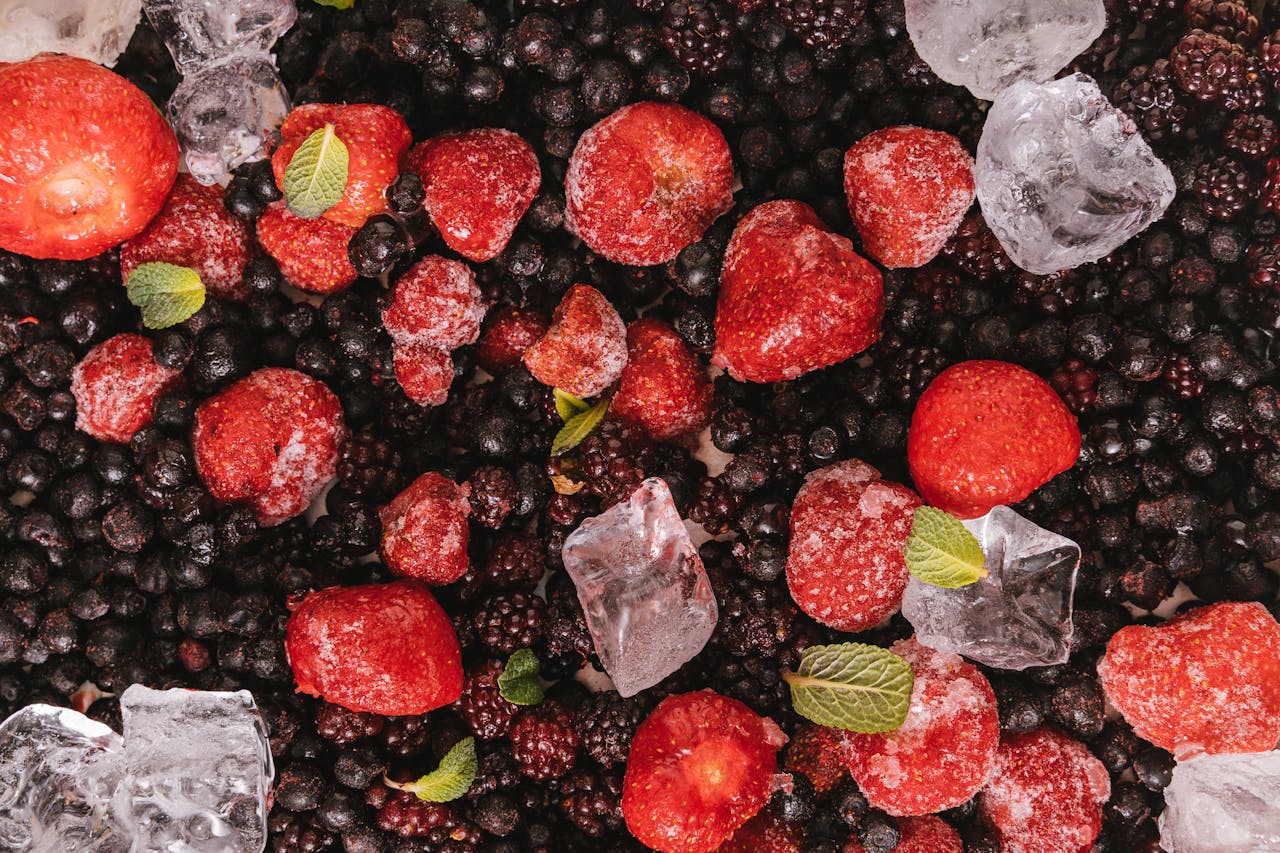 Close-up of frozen strawberries, blackberries, and blueberries with mint leaves and ice cubes.