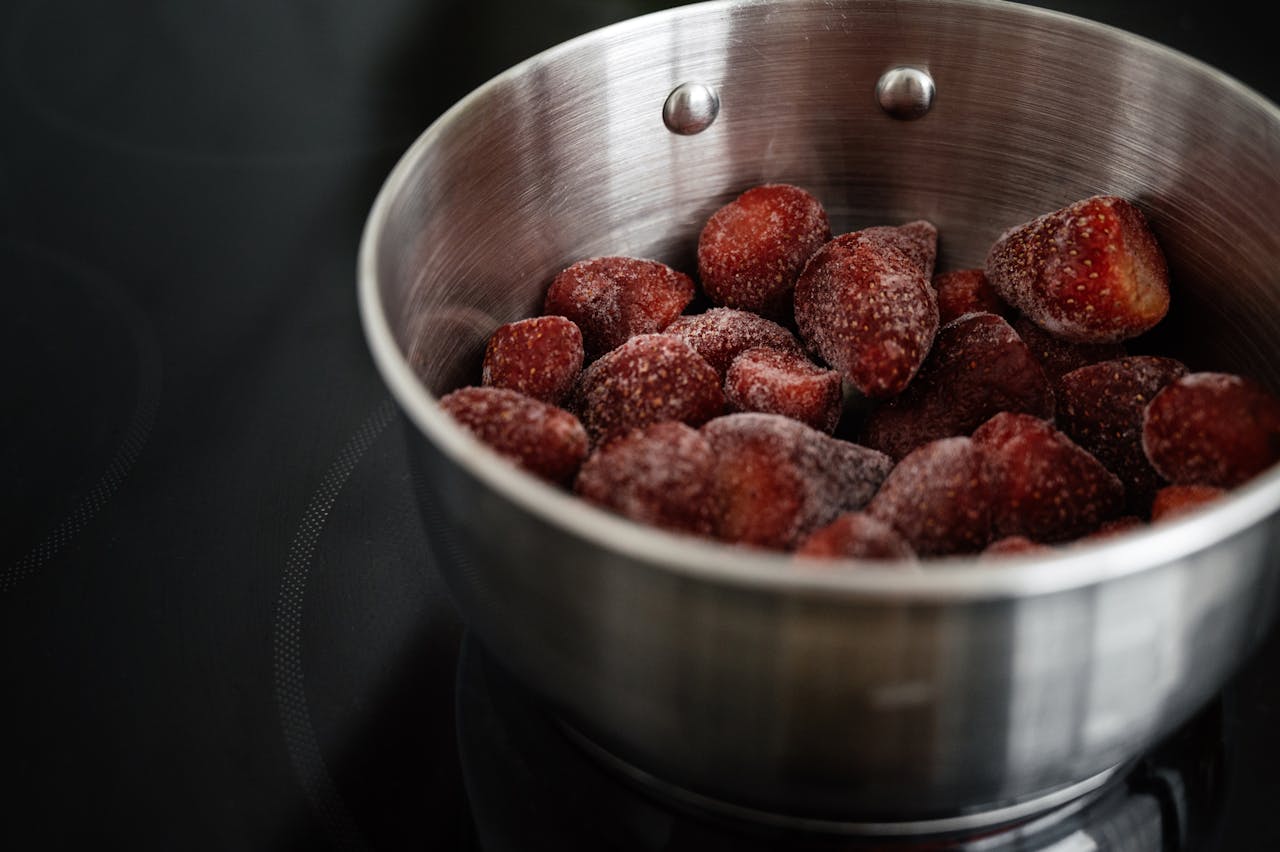 Close-up of frozen strawberries in a stainless steel pot, ready for cooking.
